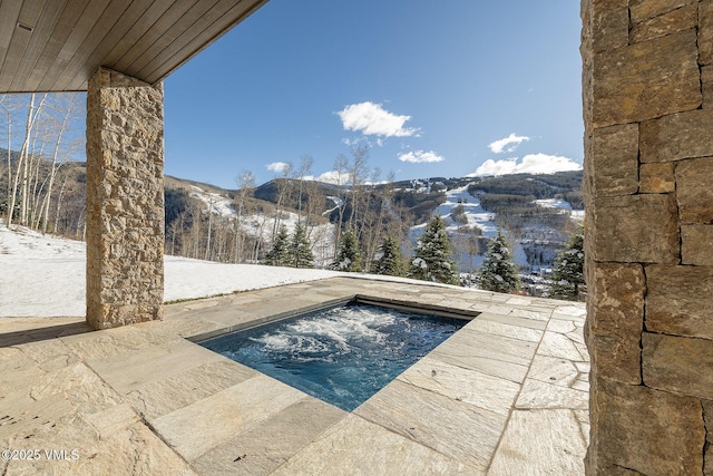 snow covered pool with a patio area and a mountain view