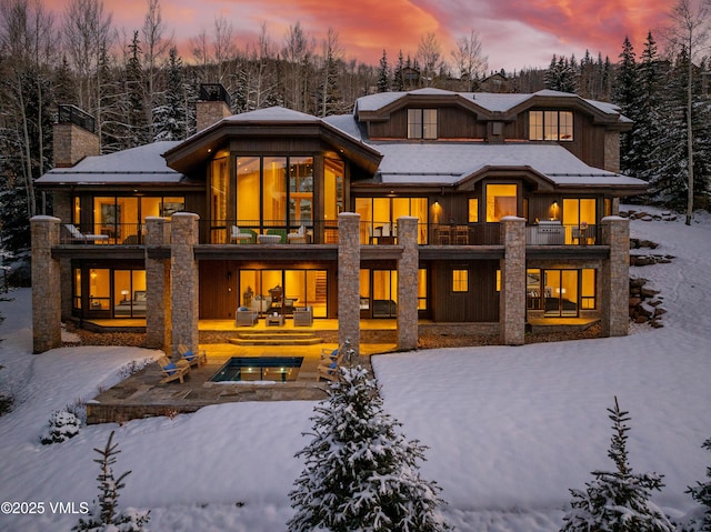 snow covered property with a chimney, an outdoor hot tub, and a balcony