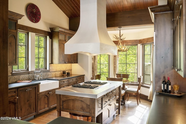 kitchen with stainless steel gas cooktop, sink, vaulted ceiling with beams, tasteful backsplash, and island range hood