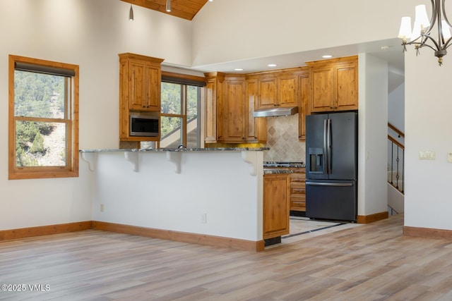 416 Eby Creek Rd, Eagle, CO 81631 - kitchen featuring black fridge with ice dispenser, light wood-style floors, stone counters, a breakfast bar area, and high vaulted ceiling