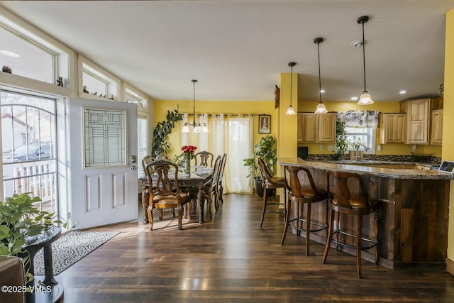 kitchen with dark stone countertops, dark wood finished floors, hanging light fixtures, a kitchen bar, and a notable chandelier