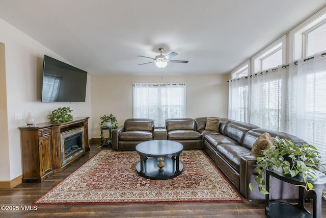 living room featuring a fireplace, baseboards, dark wood-type flooring, and a ceiling fan