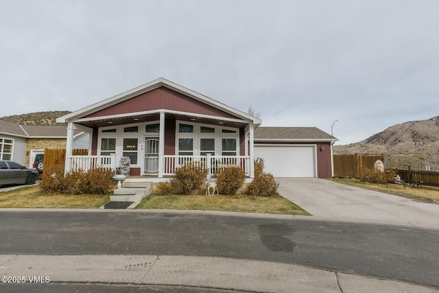 view of front facade featuring an attached garage, fence, covered porch, driveway, and a mountain view