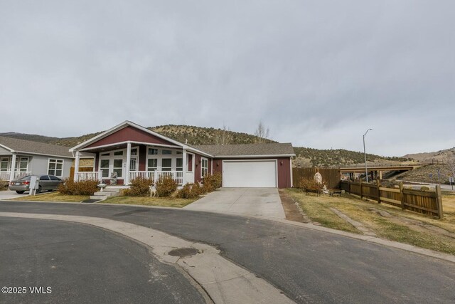 view of front of home with fence, a porch, concrete driveway, a garage, and a mountain view