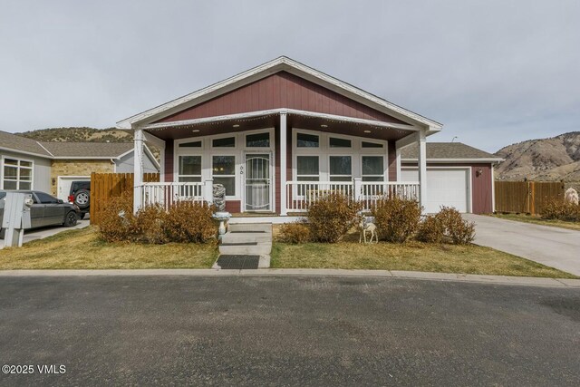 view of front of property with fence, driveway, a porch, an attached garage, and a mountain view