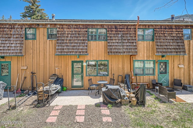 back of property with board and batten siding, a patio, and mansard roof