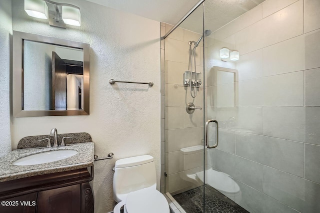 full bathroom featuring toilet, a textured wall, a shower stall, and vanity