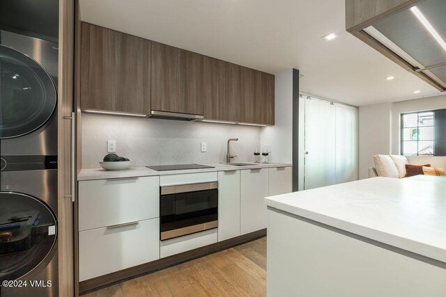 174 Gore Creek Dr Unit 268, Vail, CO 81657 - kitchen featuring oven, stacked washer / dryer, modern cabinets, a sink, and light countertops