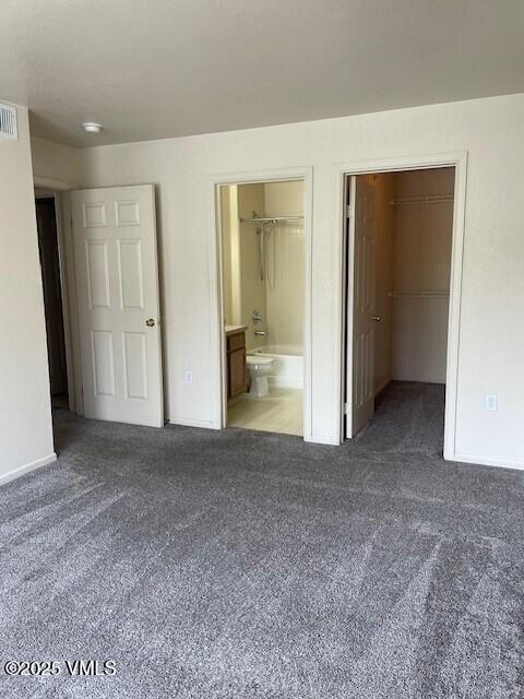 unfurnished bedroom with carpet floors, a walk in closet, ensuite bathroom, and baseboards