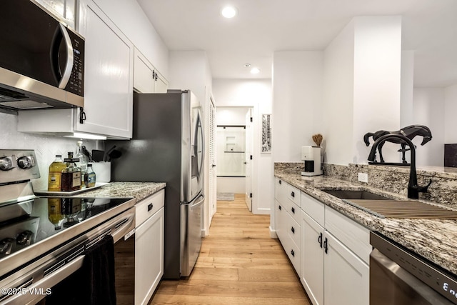 kitchen featuring stainless steel appliances, light wood-type flooring, a sink, and light stone countertops