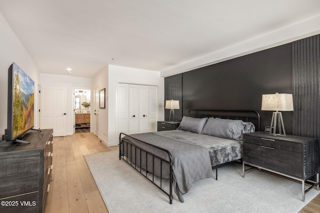 bedroom featuring light wood-type flooring, connected bathroom, an accent wall, and a closet