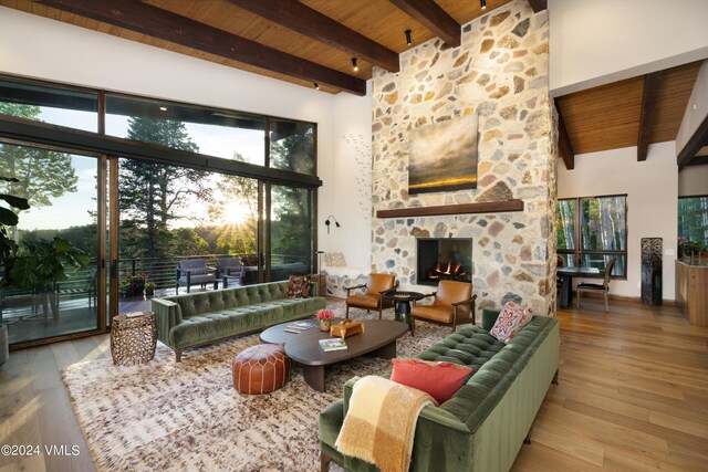 living room featuring light wood-style flooring, wooden ceiling, a stone fireplace, and a high ceiling