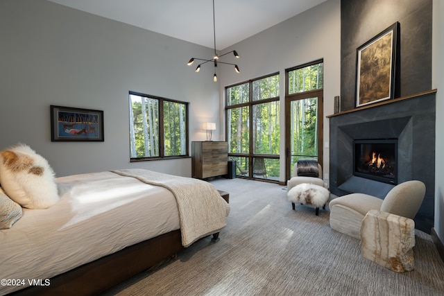 carpeted bedroom with a glass covered fireplace, a notable chandelier, and a high ceiling