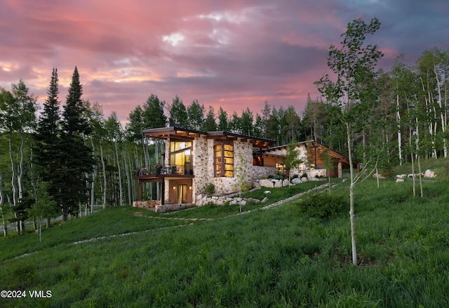 back of house featuring stone siding, a lawn, and a wooden deck