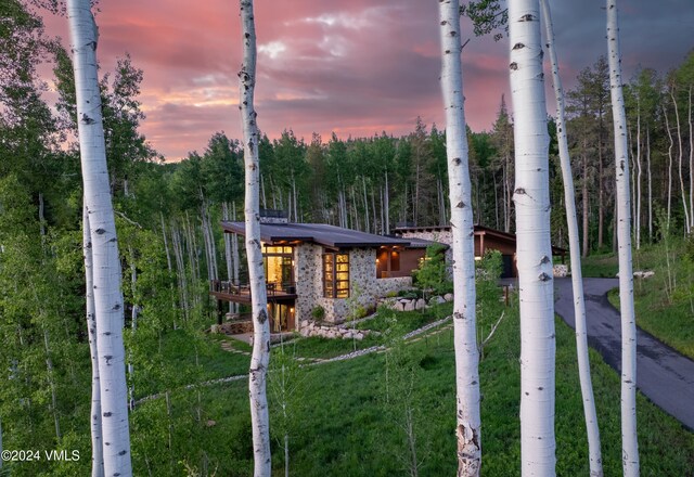 exterior space featuring a forest view, stone siding, and a lawn