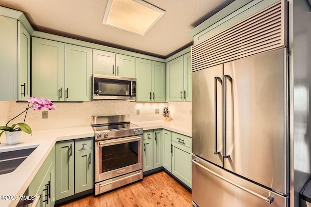1370 Sandstone Dr # 12, Vail, CO 81657 - kitchen featuring green cabinets, appliances with stainless steel finishes, light countertops, tasteful backsplash, and light wood-style floors