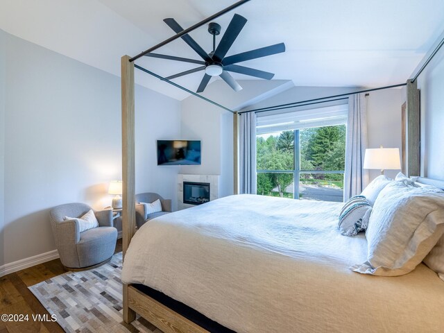 bedroom with a tiled fireplace, ceiling fan, vaulted ceiling, and wood-type flooring