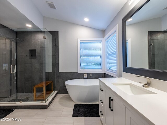 bathroom with vanity, plus walk in shower, vaulted ceiling, and tile walls