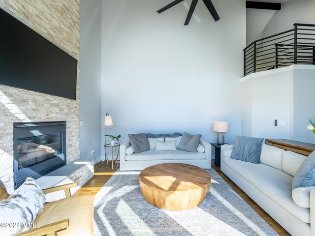 living room with ceiling fan, a towering ceiling, hardwood / wood-style floors, and a fireplace