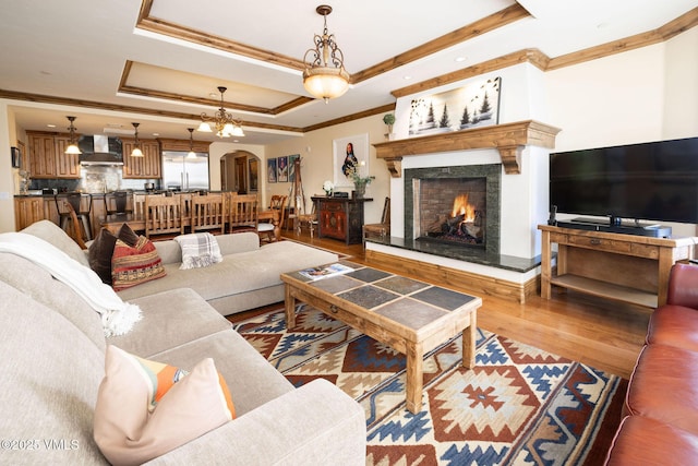 living room featuring crown molding, wood-type flooring, a raised ceiling, and a high end fireplace