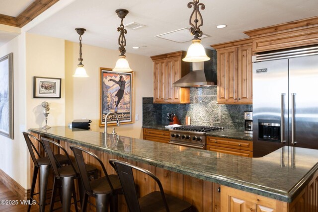 kitchen featuring a breakfast bar area, premium appliances, decorative backsplash, decorative light fixtures, and wall chimney exhaust hood