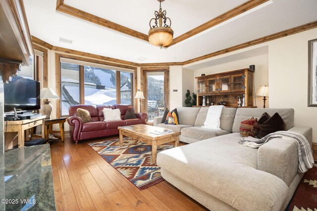 living room featuring dark wood-type flooring, ornamental molding, and a raised ceiling