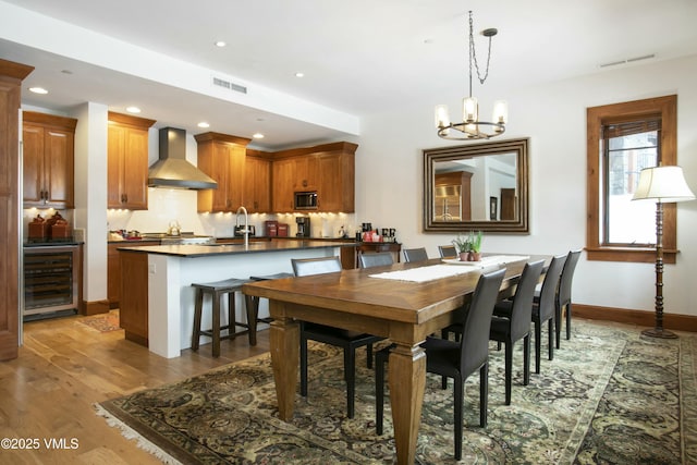 dining room featuring an inviting chandelier, sink, light hardwood / wood-style flooring, and beverage cooler