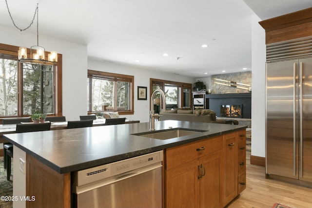 kitchen with appliances with stainless steel finishes, decorative light fixtures, sink, a kitchen island with sink, and light wood-type flooring