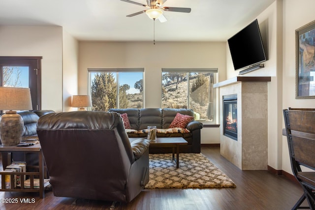 living area featuring baseboards, wood finished floors, a ceiling fan, and a tile fireplace