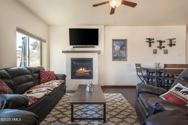 living room featuring a glass covered fireplace, wood finished floors, baseboards, and ceiling fan