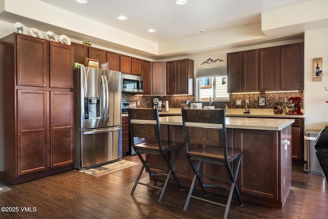 kitchen featuring dark wood-type flooring, tasteful backsplash, appliances with stainless steel finishes, and a kitchen island