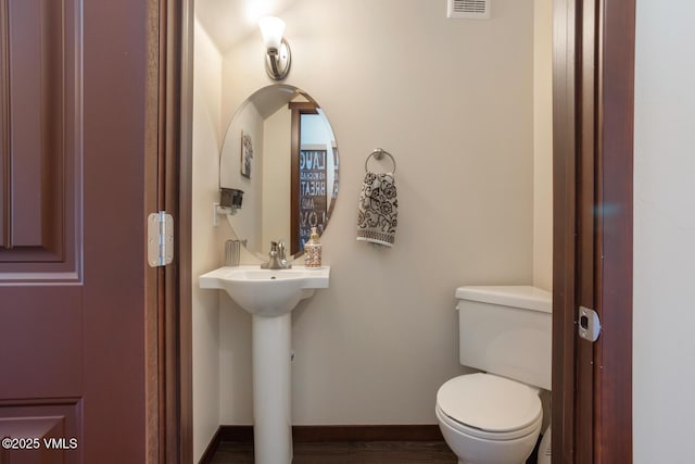 half bathroom with visible vents, baseboards, toilet, wood finished floors, and a sink