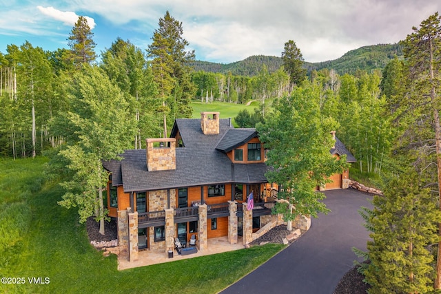 25 W Timber Draw Dr, Edwards, CO 81632 - view of front of house with a chimney, stone siding, a wooded view, and a front lawn