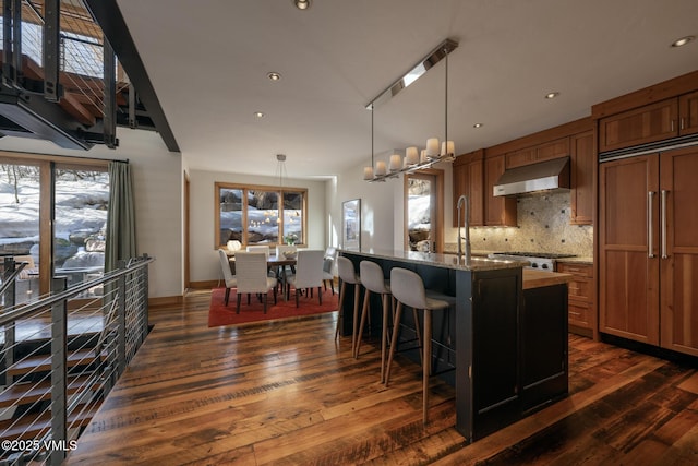 kitchen with dark wood-style floors, ventilation hood, decorative backsplash, and brown cabinets