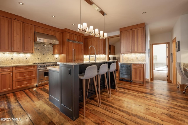 kitchen featuring brown cabinetry, range hood, wine cooler, and high end appliances