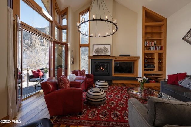 living area with hardwood / wood-style flooring, a glass covered fireplace, a wealth of natural light, and a notable chandelier