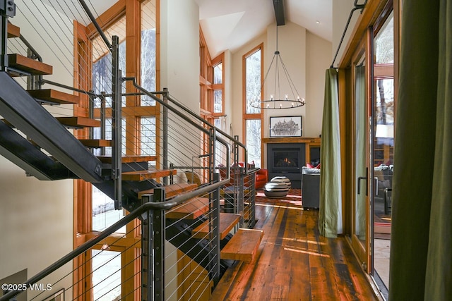 stairway featuring a chandelier, hardwood / wood-style floors, beamed ceiling, a lit fireplace, and high vaulted ceiling