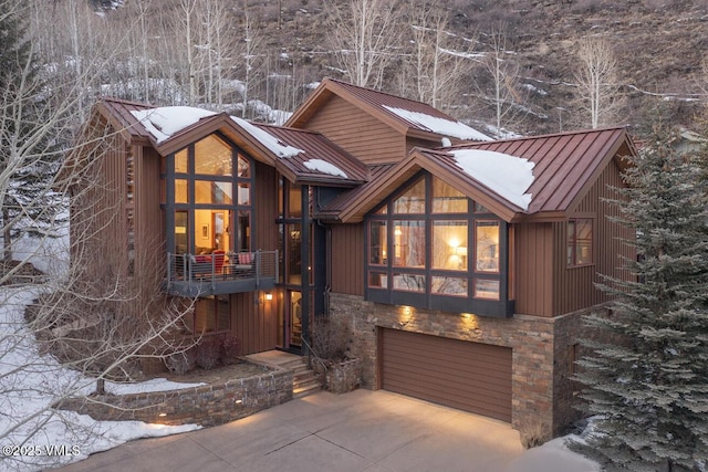 chalet / cabin featuring driveway, a garage, stone siding, metal roof, and a standing seam roof