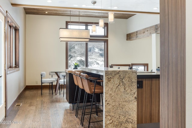 kitchen featuring baseboards, a kitchen breakfast bar, wood finished floors, decorative light fixtures, and recessed lighting