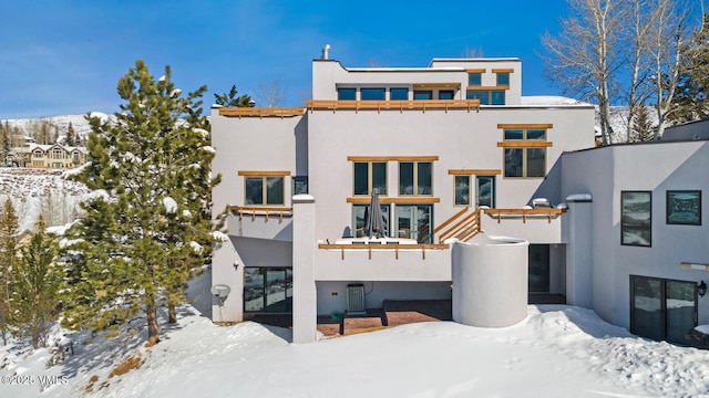 snow covered rear of property featuring stucco siding