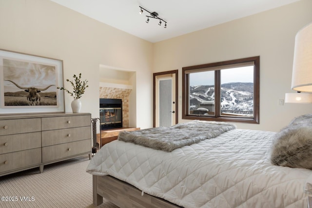 bedroom with track lighting, light colored carpet, a mountain view, and a fireplace