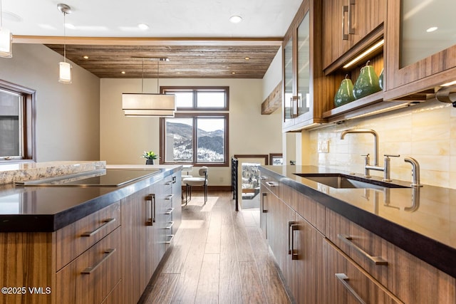 kitchen featuring a sink, brown cabinets, dark countertops, glass insert cabinets, and pendant lighting