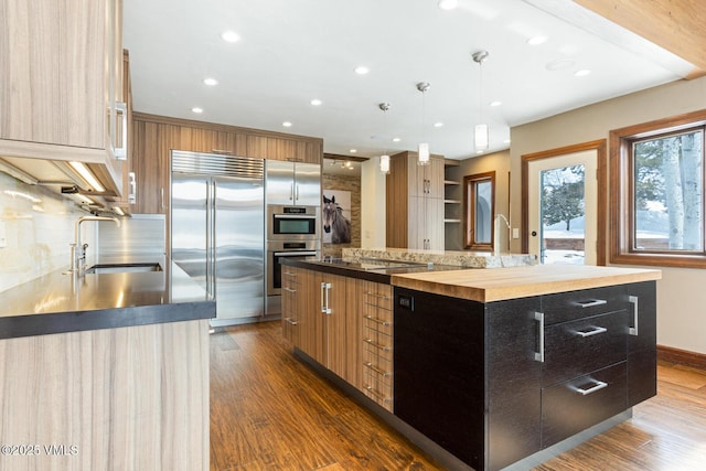 kitchen featuring a sink, hanging light fixtures, appliances with stainless steel finishes, dark cabinetry, and a center island