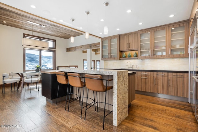 kitchen featuring glass insert cabinets, brown cabinets, and decorative light fixtures