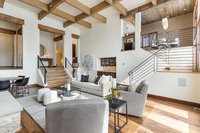 living area featuring baseboards, stairway, light wood-style flooring, and beam ceiling