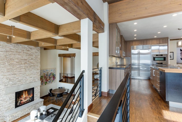 kitchen featuring dark wood-style floors, stainless steel built in fridge, a sink, modern cabinets, and beamed ceiling