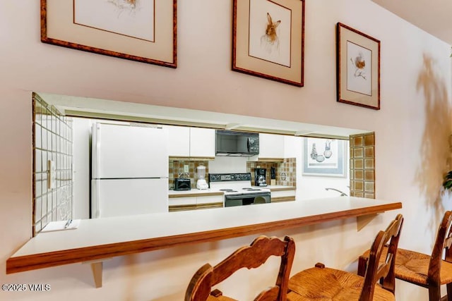 kitchen featuring white cabinets, white appliances, a breakfast bar, and light countertops