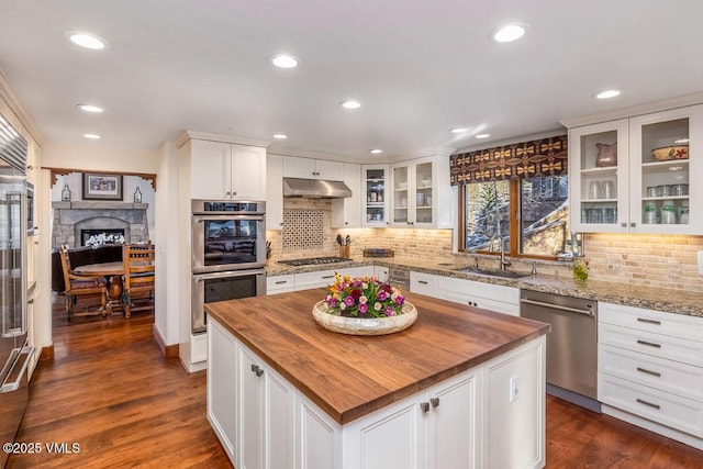 kitchen with under cabinet range hood, butcher block countertops, white cabinets, stainless steel appliances, and a sink