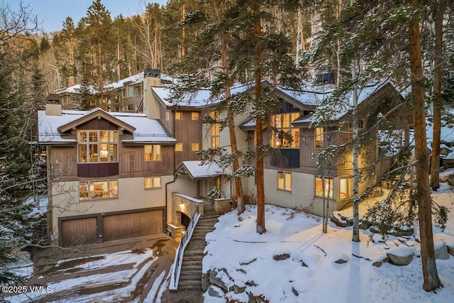 rustic home with stairway, stucco siding, a chimney, and a garage