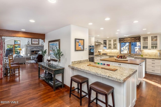 kitchen with tasteful backsplash, stainless steel double oven, a fireplace, wooden counters, and dark wood-style flooring